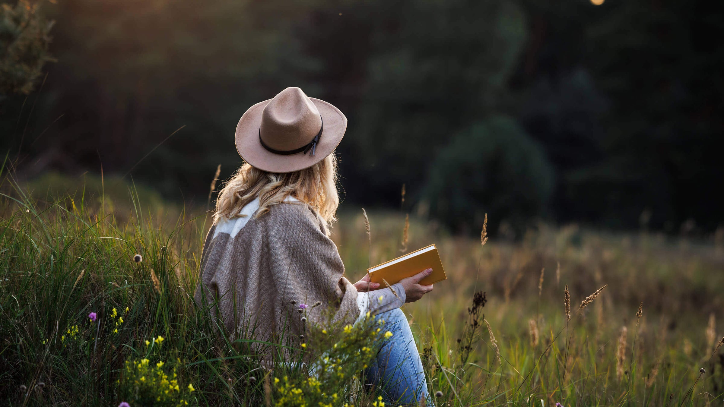 Woman is relaxing in nature and reading a book to improve her mindfulness and mental health.