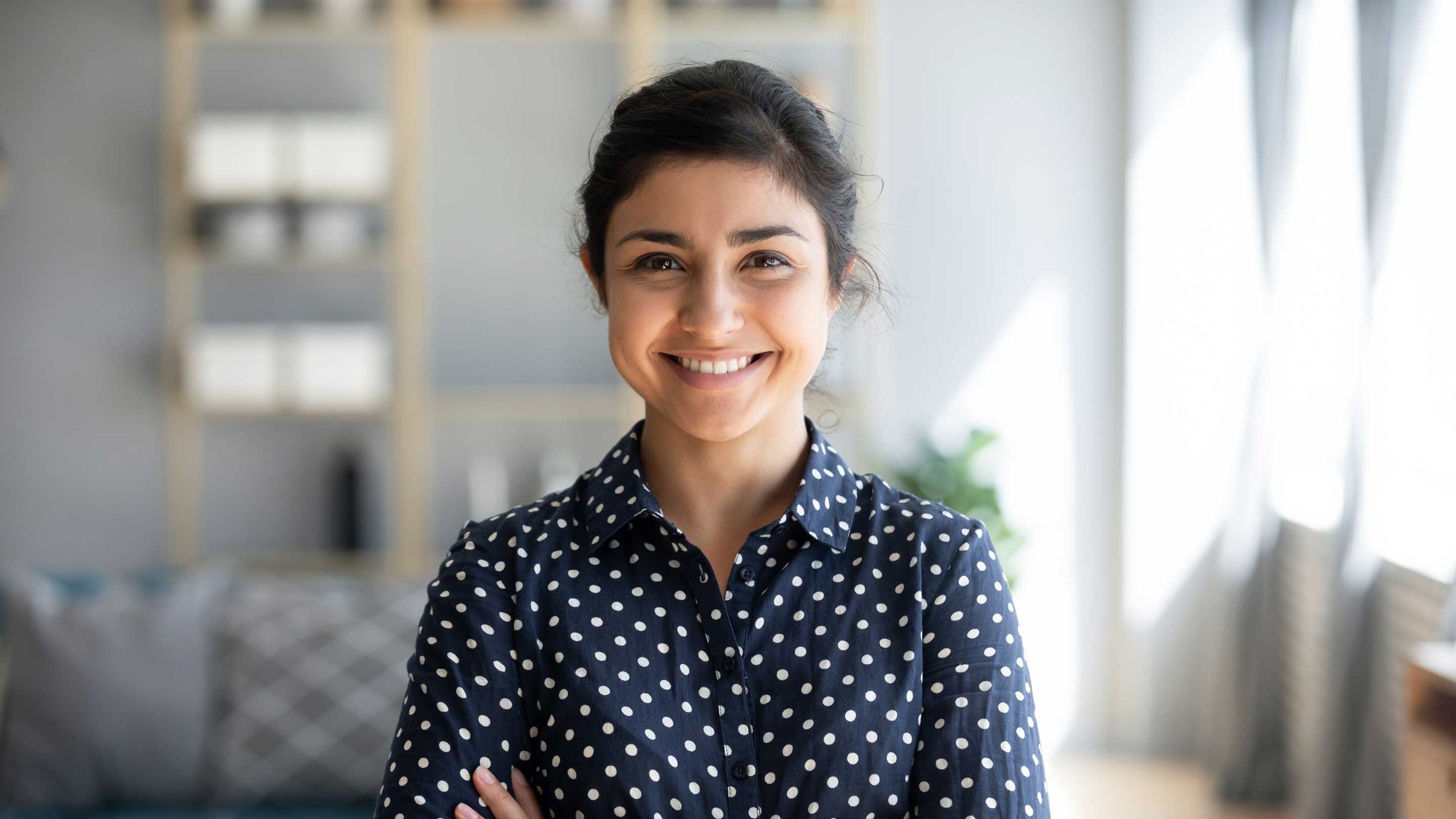 Confident smiling millennial indian woman standing with folded arms.